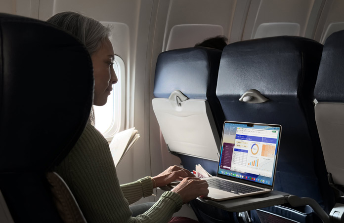 En person som sitter i en flygplansstol och jobbar på sin MacBook Air