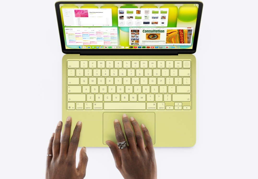 MacBook Neo i farven citrus med en persons hånd på pegefeltet og flere åbne vinduer, herunder de tre apps Musik, Kalender og Microsoft PowerPoint