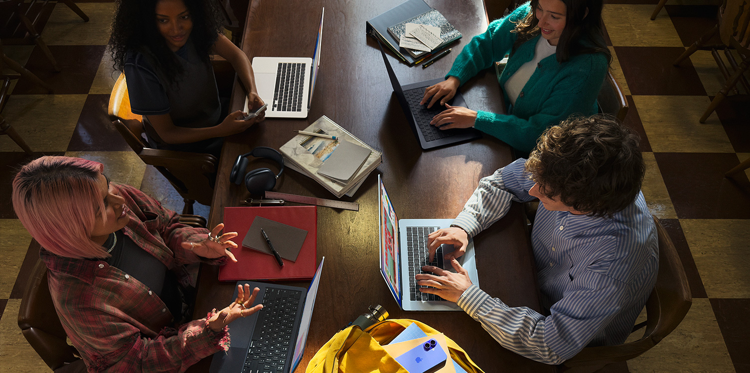 テーブルに向かって座る4人の学生。学生たちの前にはMacBookが開かれており、ノートが置かれている