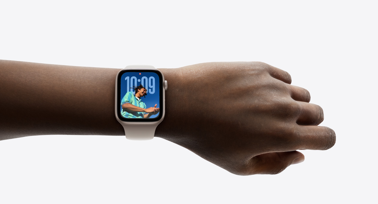 特寫手腕上戴著搭配橡膠錶帶的玫瑰金色 Apple Watch，錶面展示以全新 Liquid Glass 設計呈現的時鐘 app