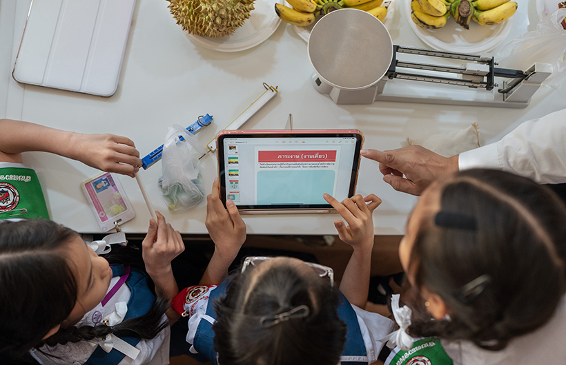 นักเรียนชั้นประถมศึกษา 3 คน นั่งล้อม iPad เพื่อช่วยกันทำงานนำเสนอโครงงานวิทยาศาสตร์