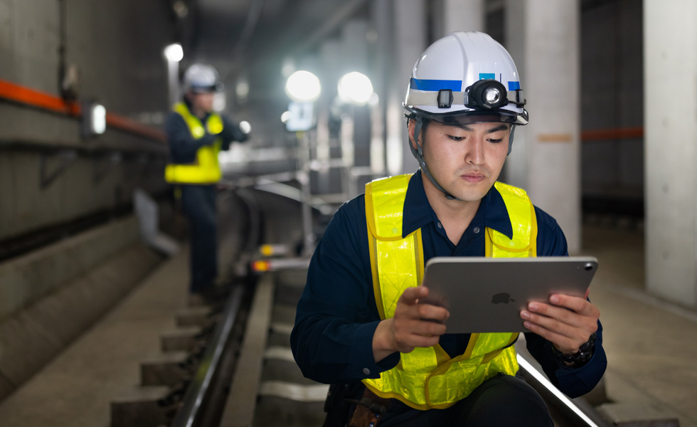 Um trabalhador de colete e capacete de segurança usa um iPad durante a manutenção nos túneis do metrô de Tóquio.