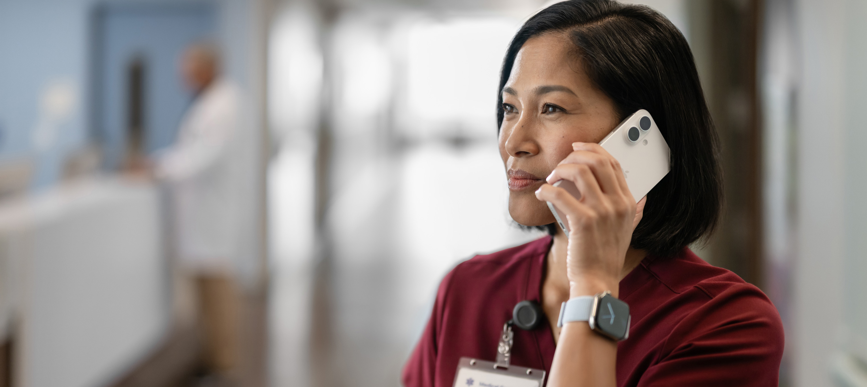 Eine weibliche Pflegekraft in roter Arbeitskleidung, die mit ihrem iPhone telefoniert.