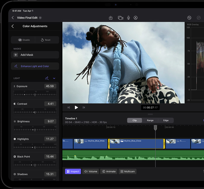 iPad Pro, face avant, cadre d’écran noir, écran affichant une app de montage vidéo avec la photo d’une mannequin vêtue d’un manteau bleu et d’un pantalon imprimé noir et blanc, panneau d’ajustement des couleurs ouvert sur la gauche avec divers effets vidéo et curseurs, timeline en bas avec plusieurs plans vidéo et pistes audio