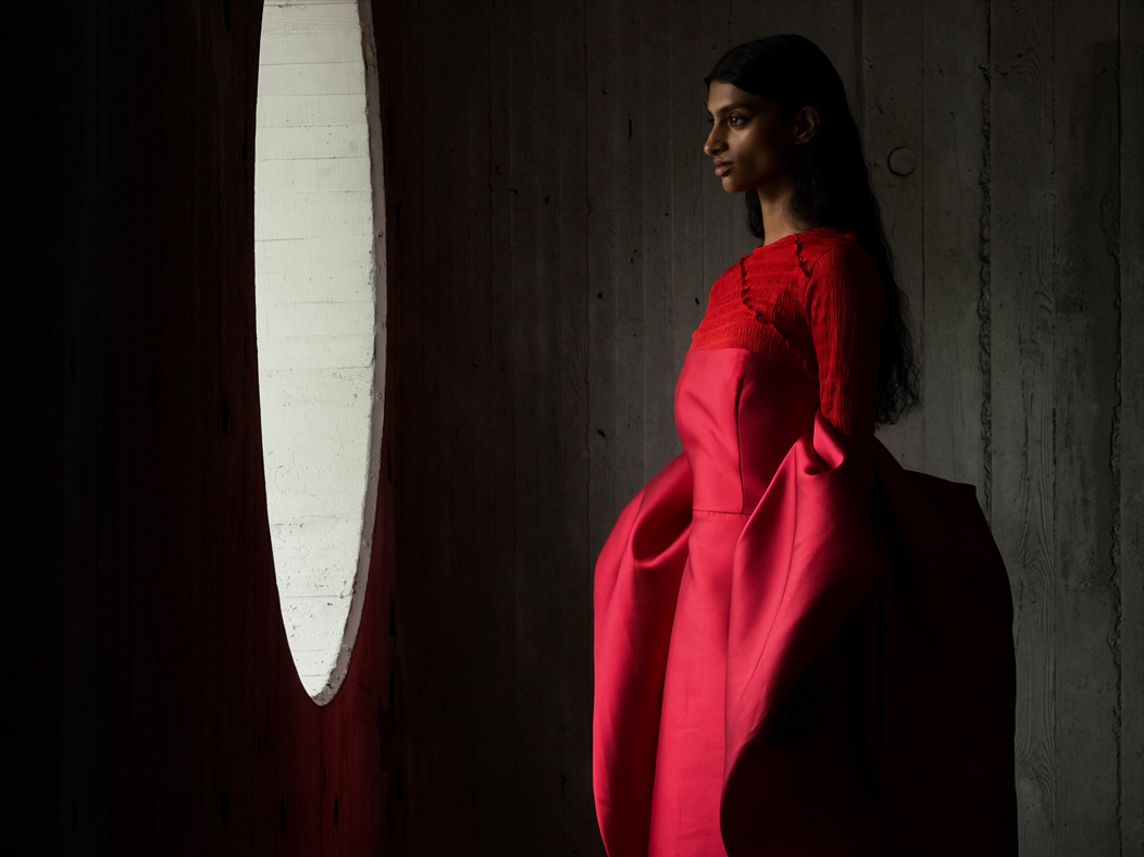 Una donna con un lungo vestito rosso fotografata in piedi in una stanza vuota. Nell’app Foto la lunghezza focale viene regolata a 200 mm, per mettere in evidenza le capacità del sistema di fotocamere Pro