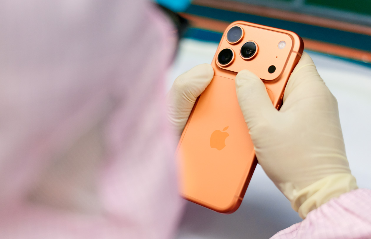 พนักงานในชุดคลุมแบบเต็มตัวกำลังตรวจสอบ iPhone ที่เวิร์กสเตชั่น