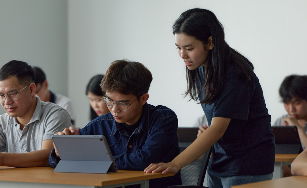 คนสองคนในห้องเรียนกำลังทำงานร่วมกันบนแท็บเล็ต Apple